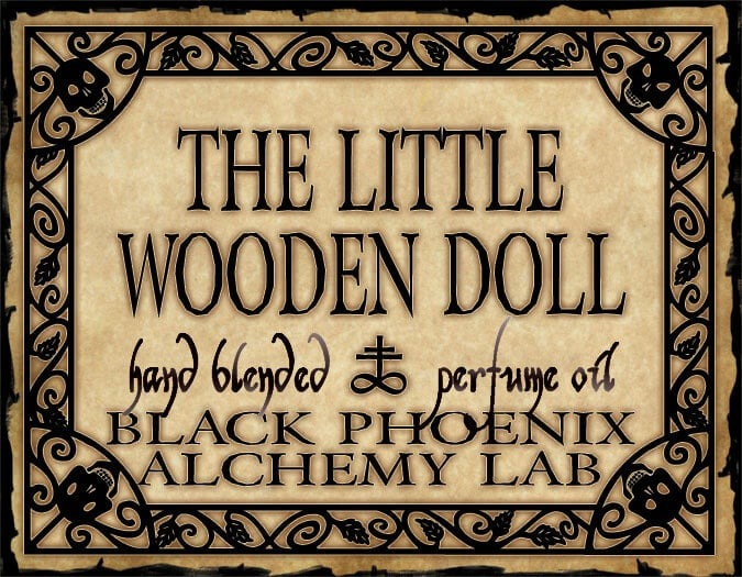 Label for 'The Little Wooden Doll' perfume oil by Black Phoenix Alchemy Lab with decorative border.