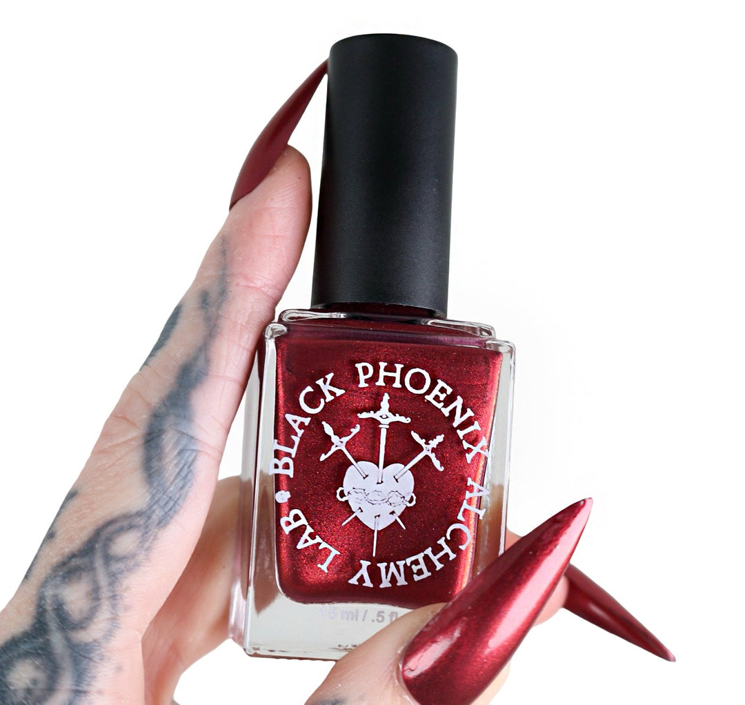 Red nail polish bottle with black cap held by a hand with red nails on a white background