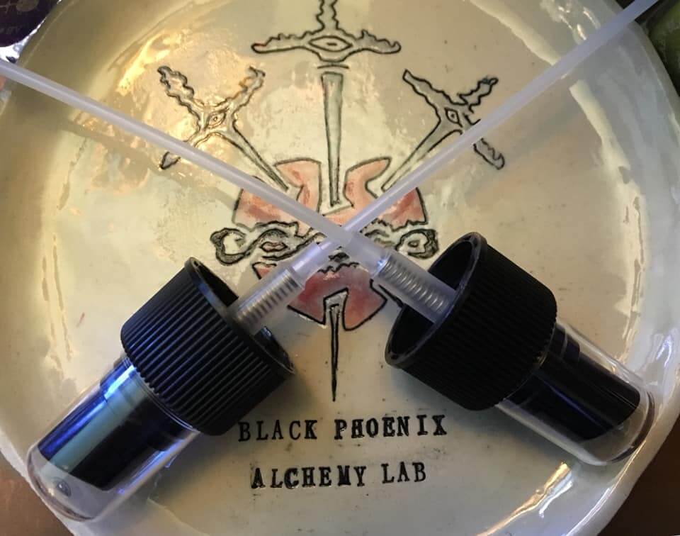 Two small bottles with black caps on a white plate with 'Black Phoenix Alchemy Lab' branding.