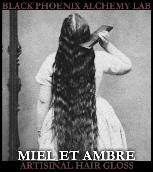 Person with long hair combing their hair, with 'Black Phoenix Alchemy Lab' and 'Miel et Ambre Artisinal Hair Gloss' text.