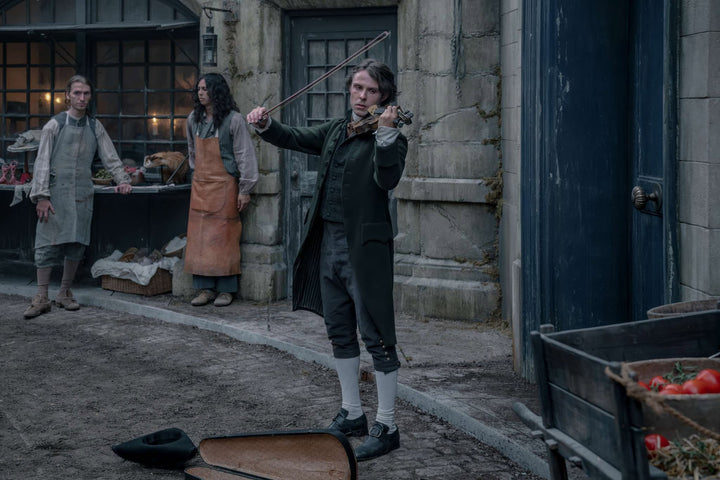 Nicolas de Lenfent busking on a cobblestone street in period costume — The Vampire Lestat x AMC, Interview with the Vampire Season 3
