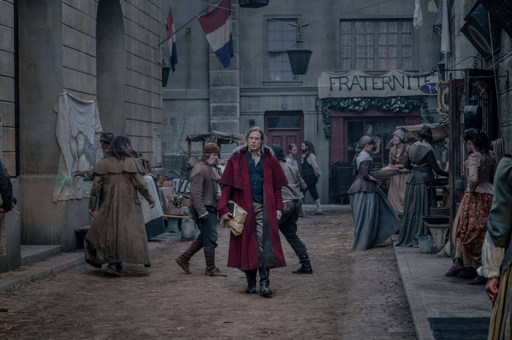  Lestat de Lioncourt in red velvet coat striding through a Revolutionary Paris street market —The Vampire Lestat x AMC, Interview with the Vampire Season 3
