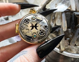 photograph of BPAL's Pisces steampunk astrological scent locket held in a hand with long nails